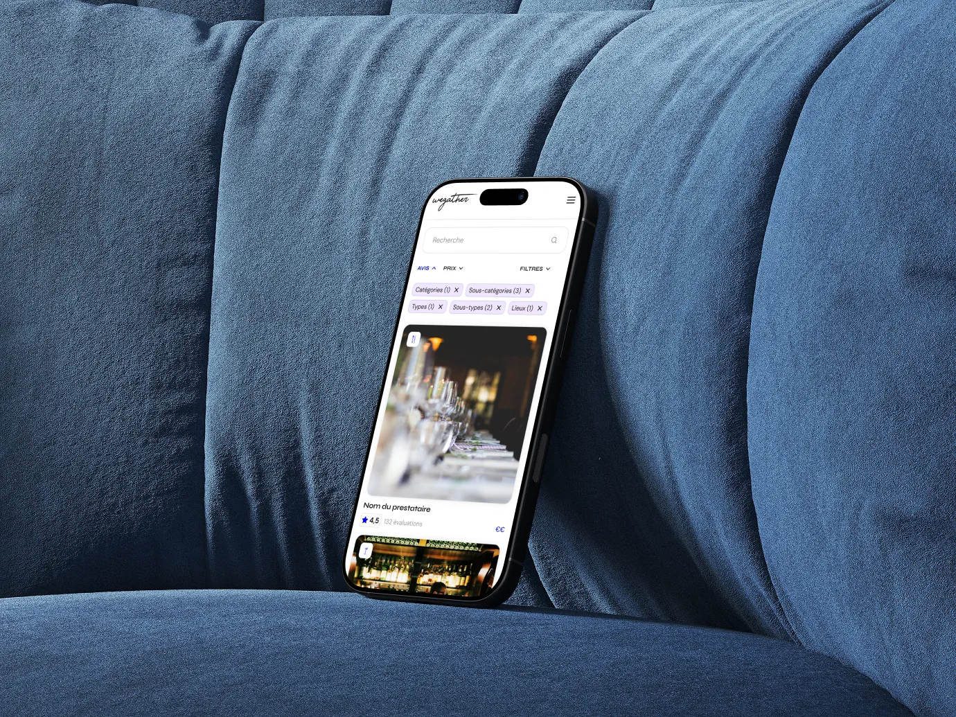 Smartphone displaying a restaurant review app in French, resting on a blue textured couch; the screen shows filtered search options and ratings.