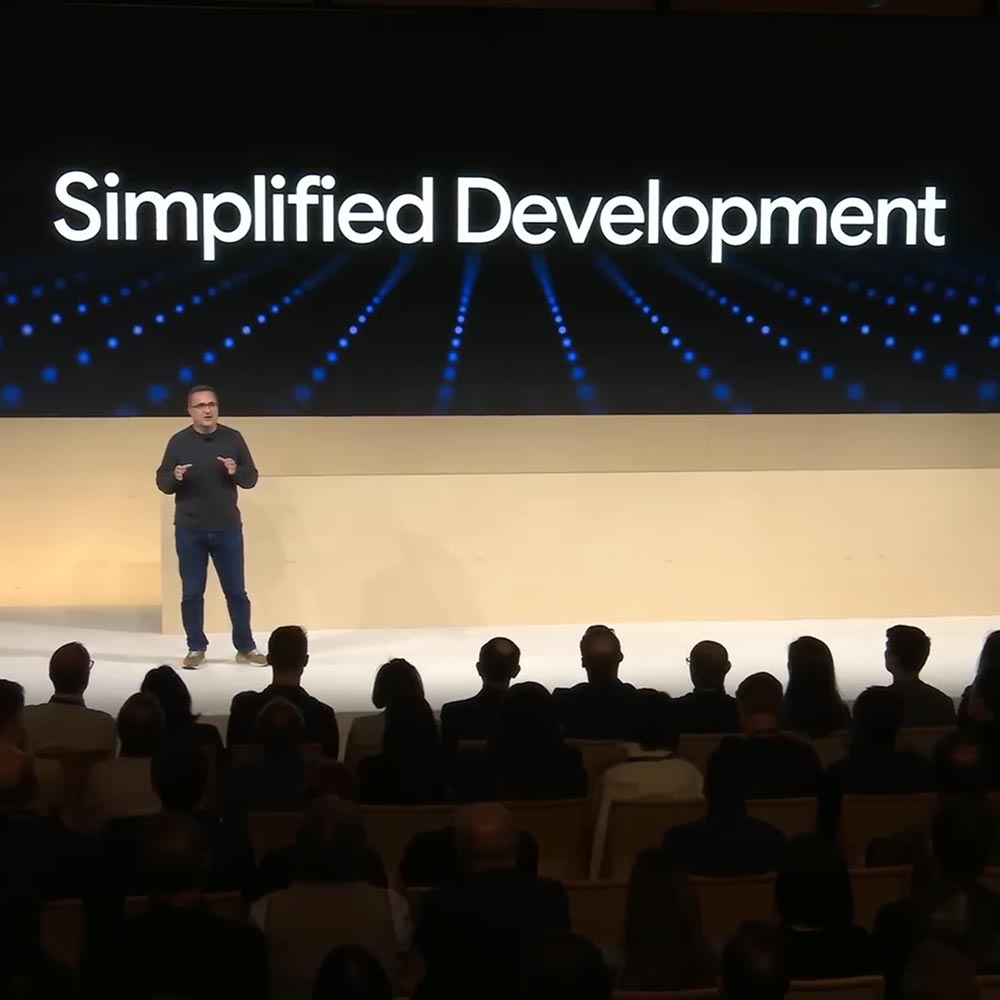 A male speaker stands onstage at the XR Unlocked event in front of a screen that reads "Simplified Development."