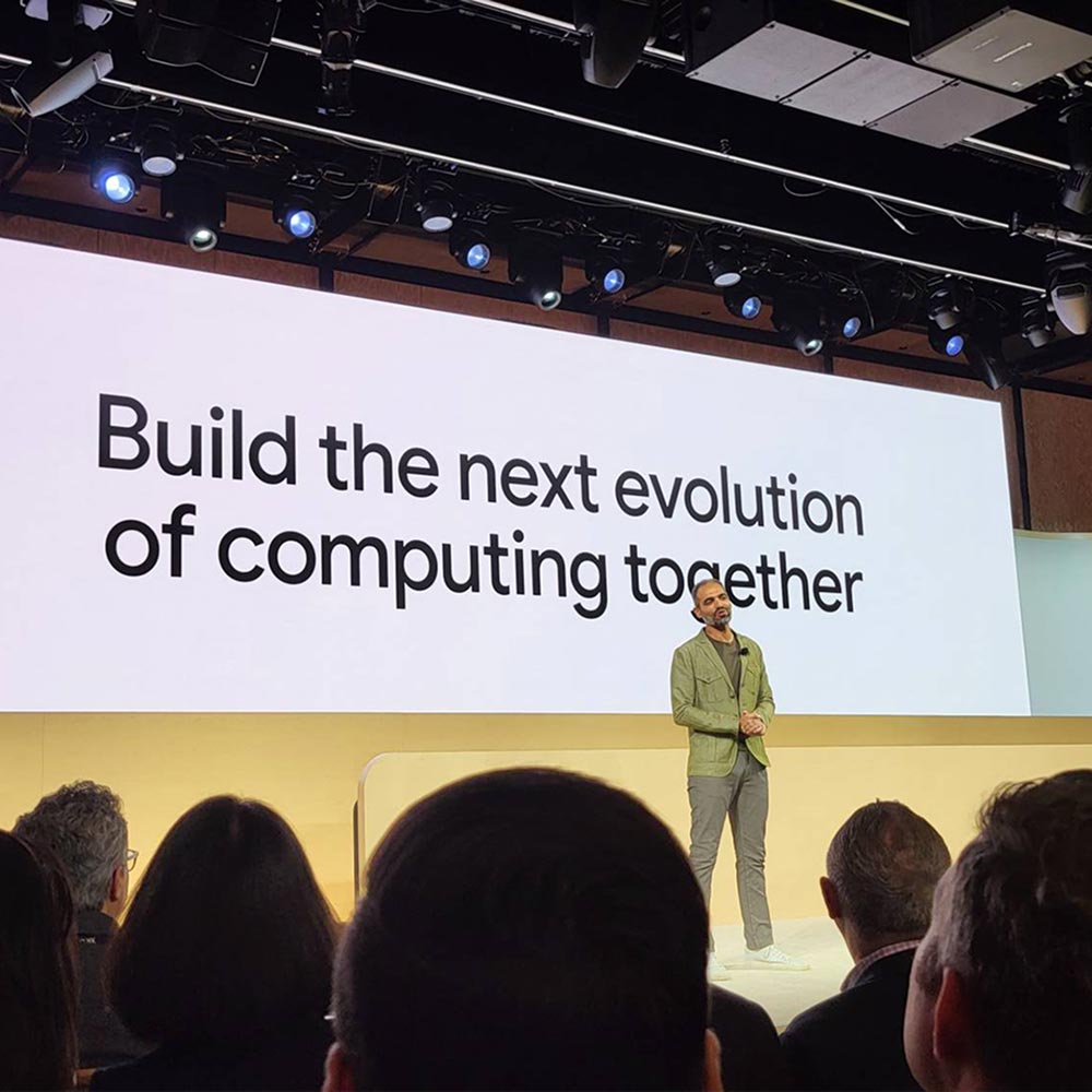 A speaker stands onstage at XR Unlocked in front of a screen that reads "Build the next evolution of computing together."