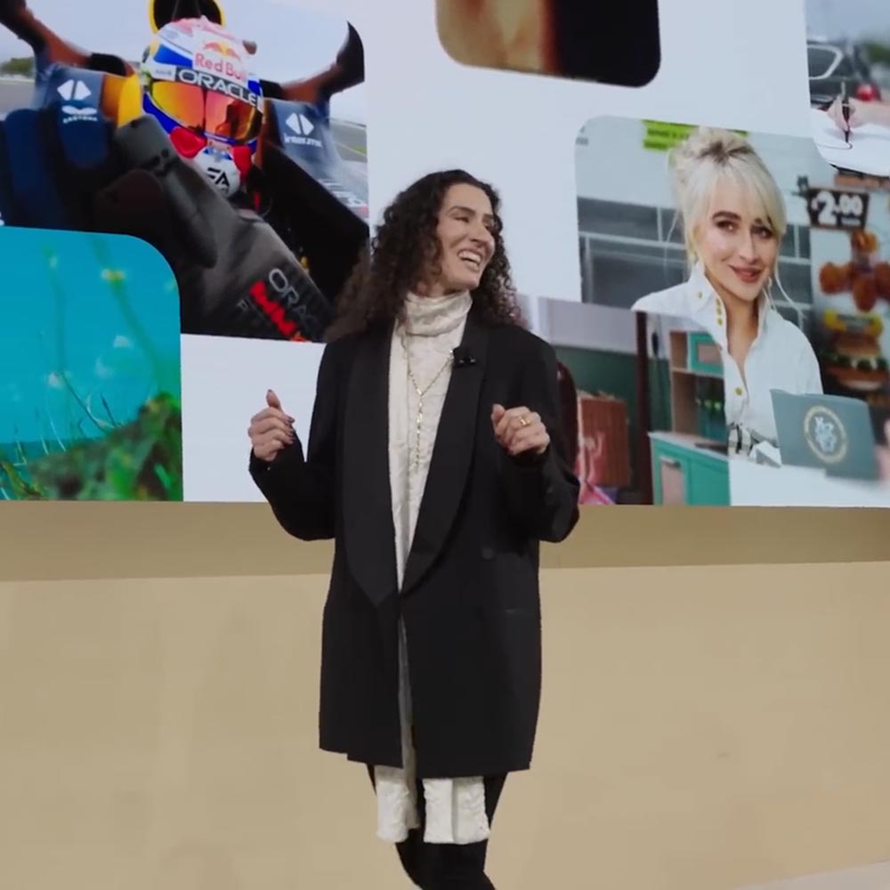A female speaker stands onstage at XR Unlocked in front of a collage of photography. 