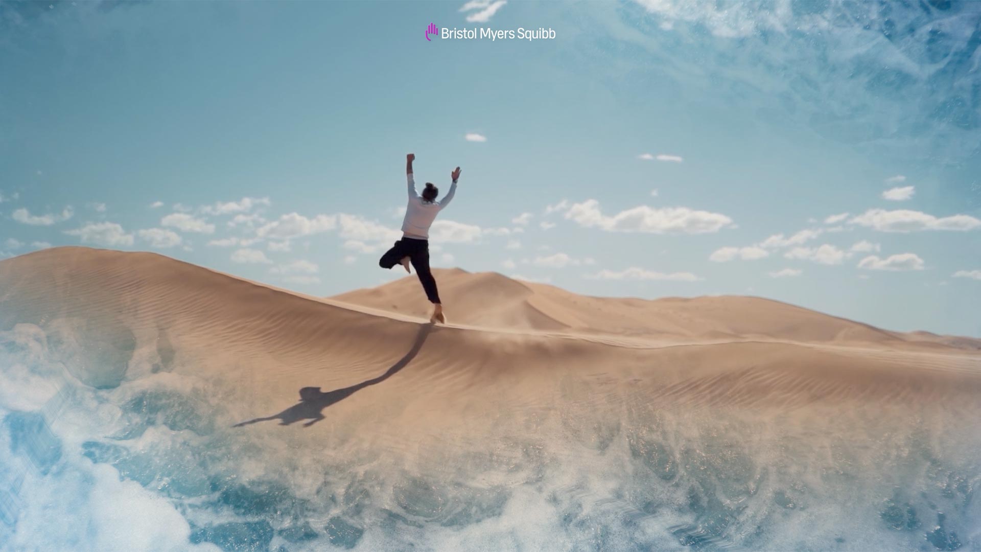 A man jumps on sand dunes with images of the ocean in the corner of the frame. Text reads "Bristol Myers Squibb."