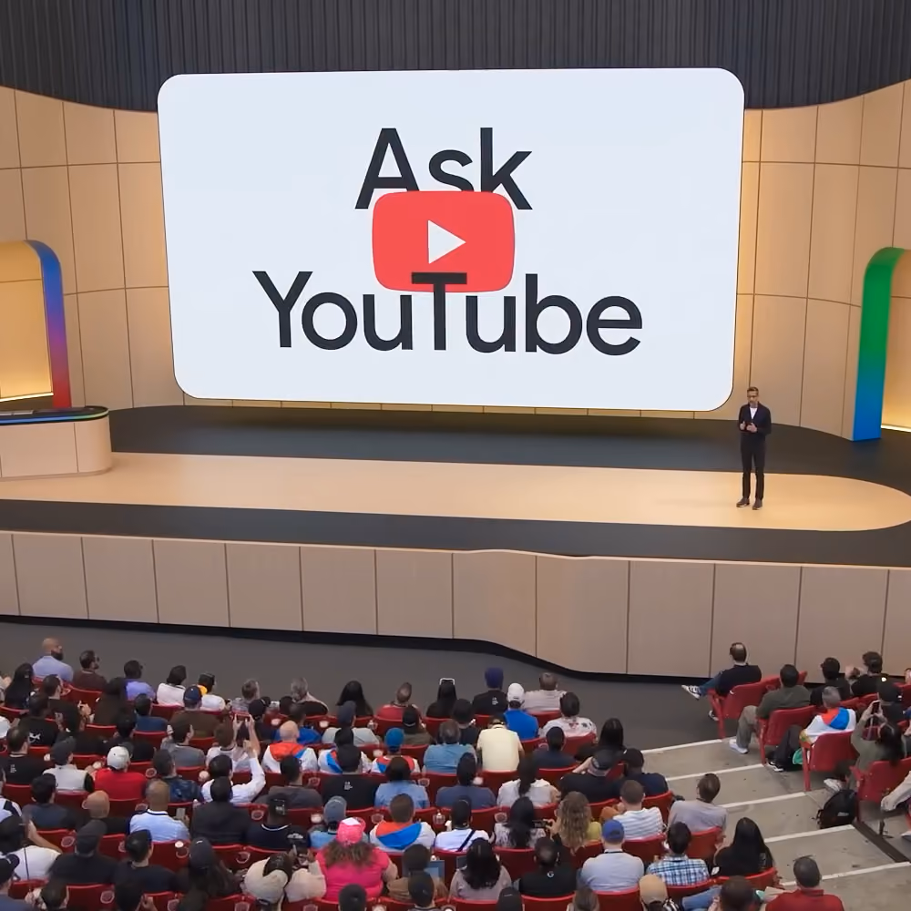 Sundar Pichai on stage at Google I/O in front of an audience, with “Ask YouTube” displayed onscreen.