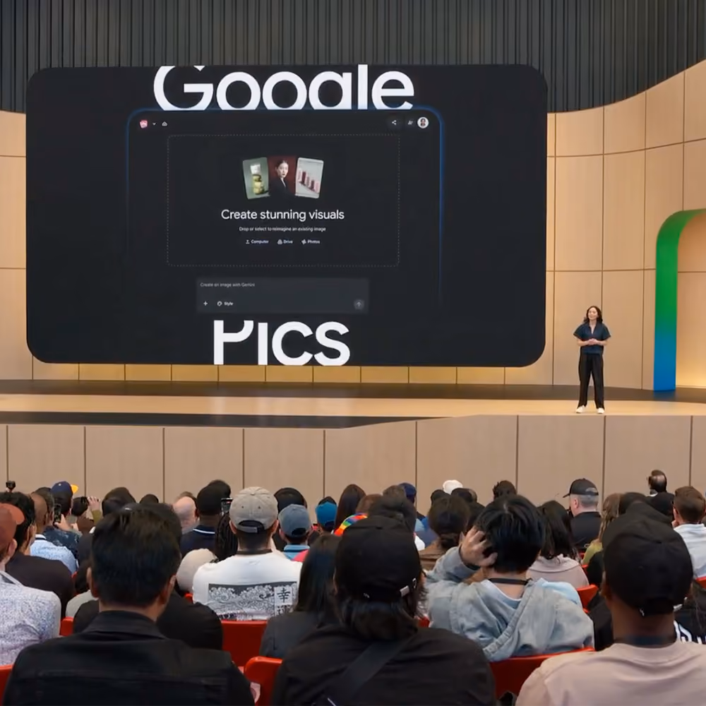 A speaker on stage at Google I/O in front of an audience, with a large screen displaying a Google Pics interface mockup.
