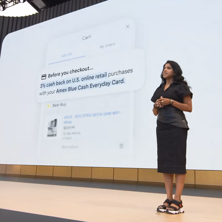 Speaker on stage at Google I/O before a screen displaying a shopping cart with an Amex cash back notification.