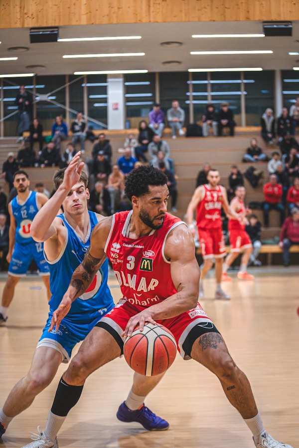 Basketball player in red jersey dribbles ball past defender