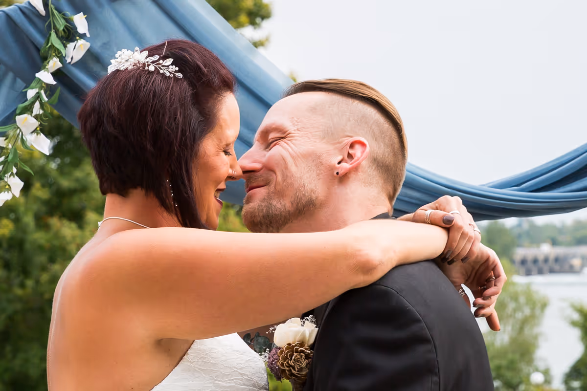 Bride and groom embracing closely with eyes closed during outdoor wedding ceremony.