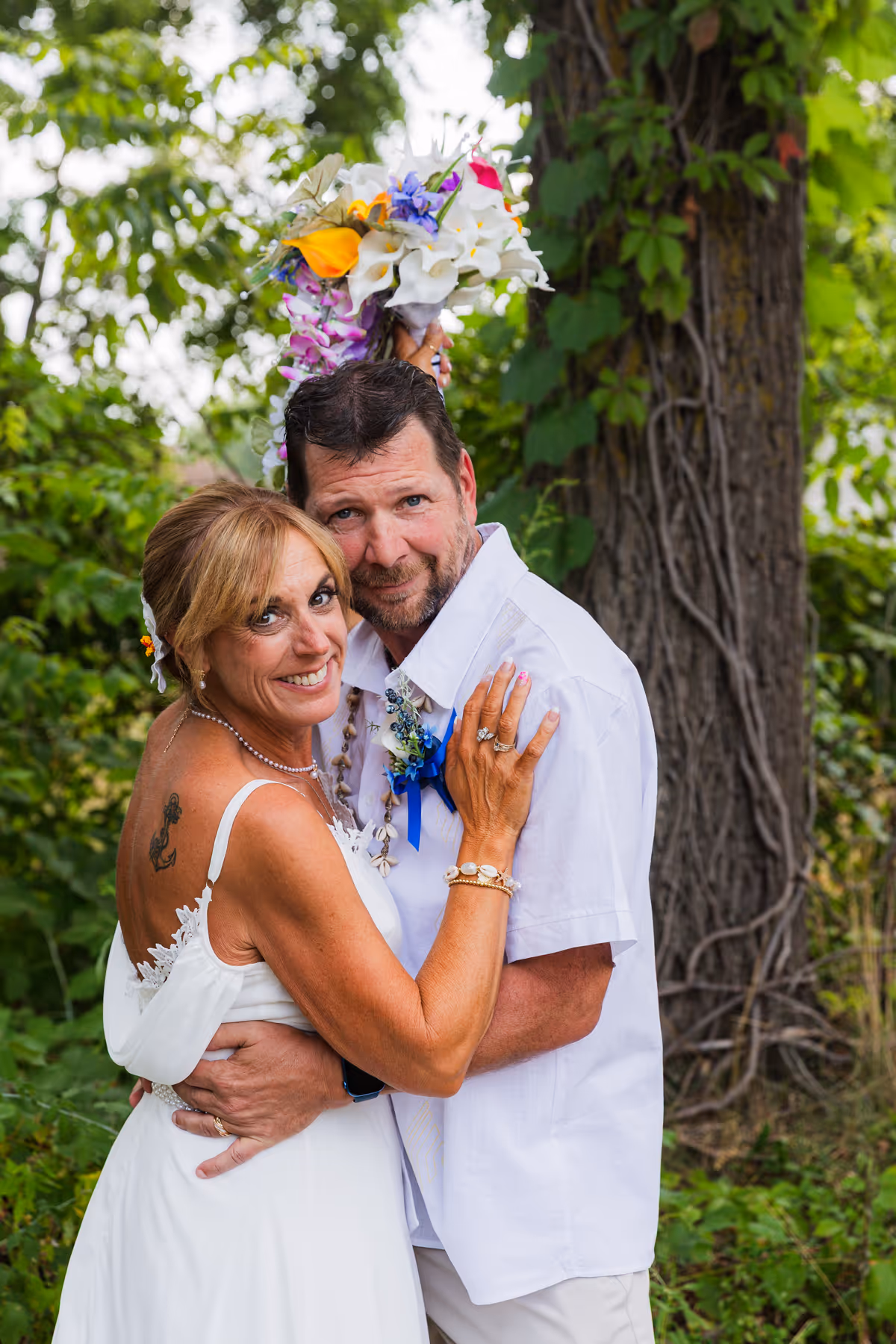 Bride and groom embracing outdoors, smiling, with bride holding a colorful flower bouquet.