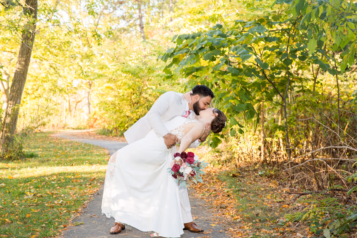 Bride and groom kissing on a forest path with the groom dipping the bride holding a bouquet.