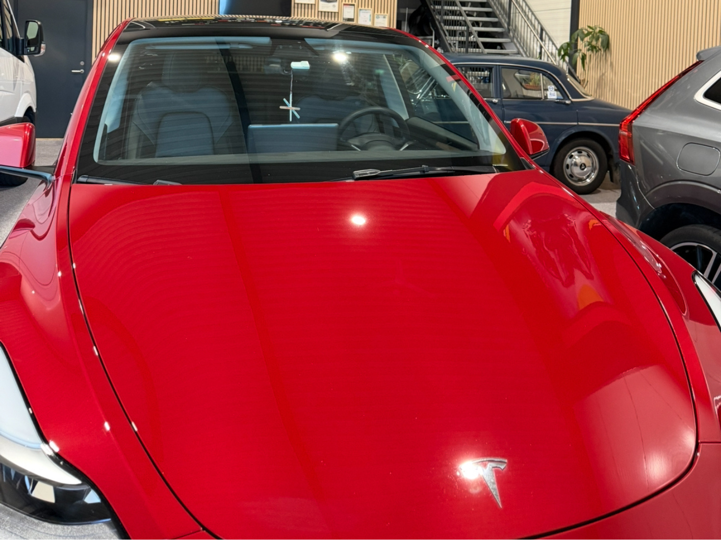 Rød Tesla-elbil parkert innendørs med synlig ratt og frontrute.