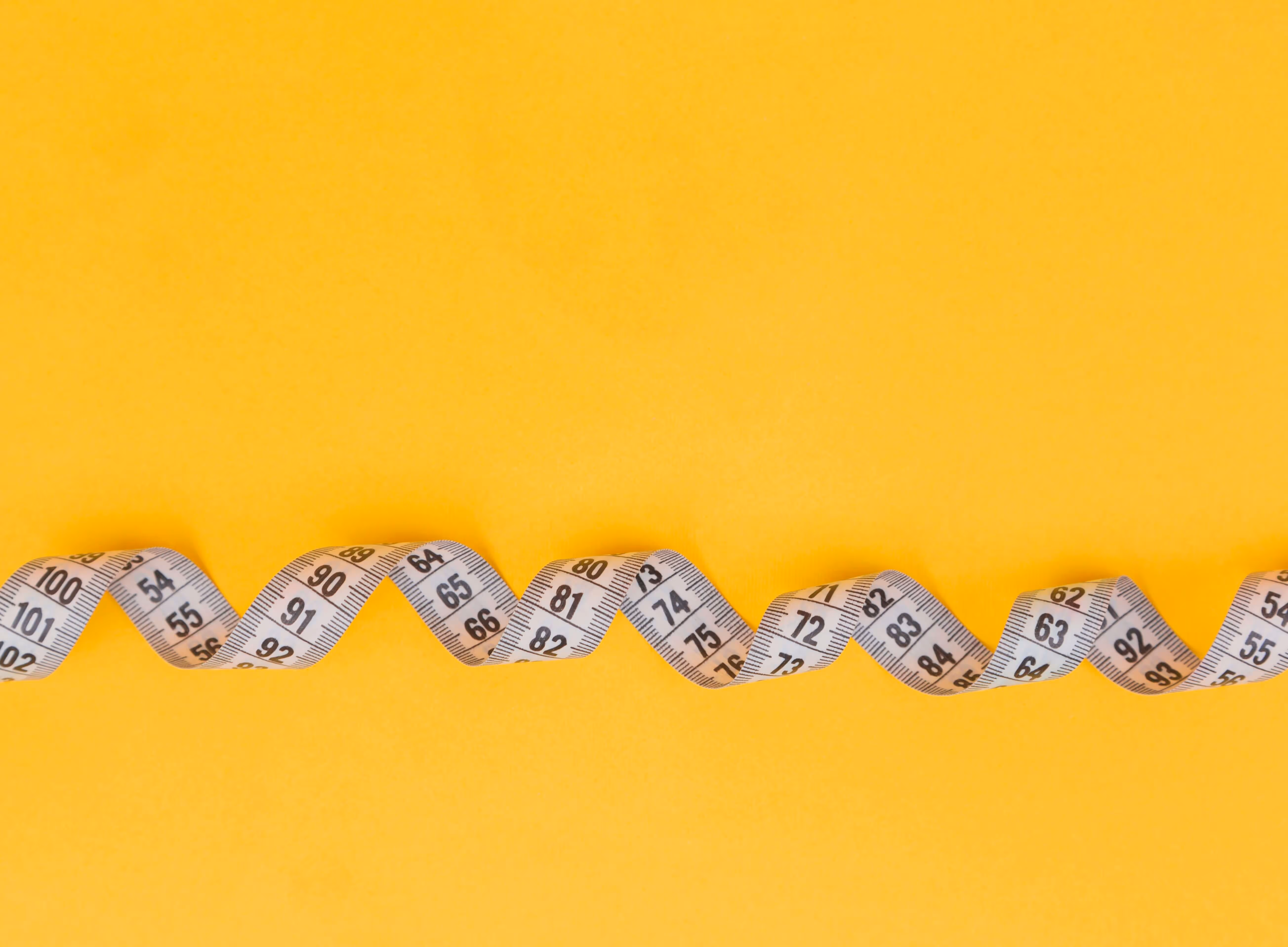 Measuring tape twirling with a yellow background