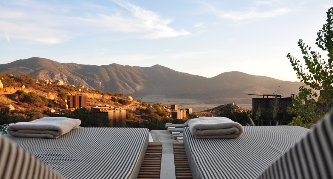 Two lounge chairs with striped covers overlooking a valley during sunset.