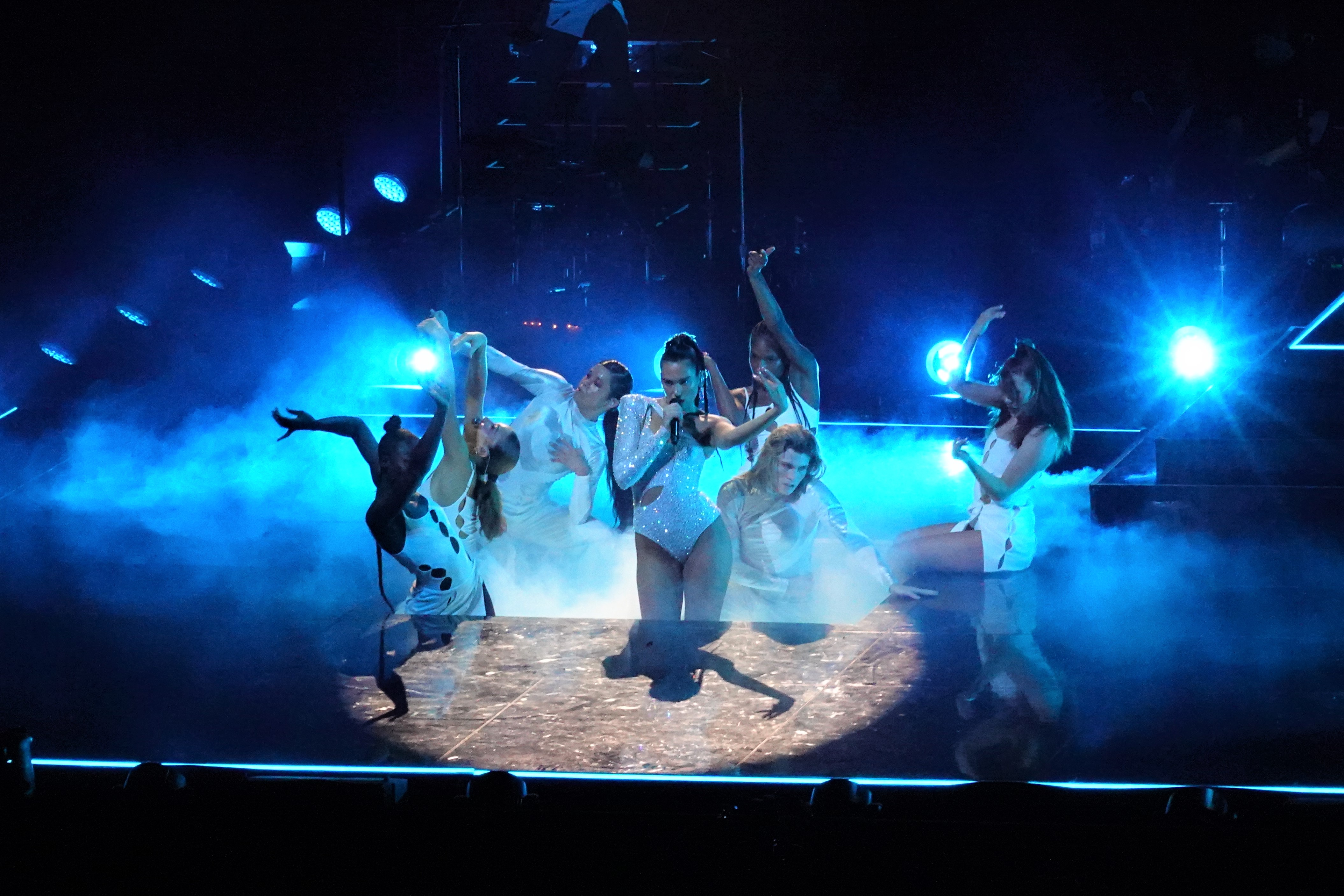 Lead singer with backup dancers performing in the spotlight