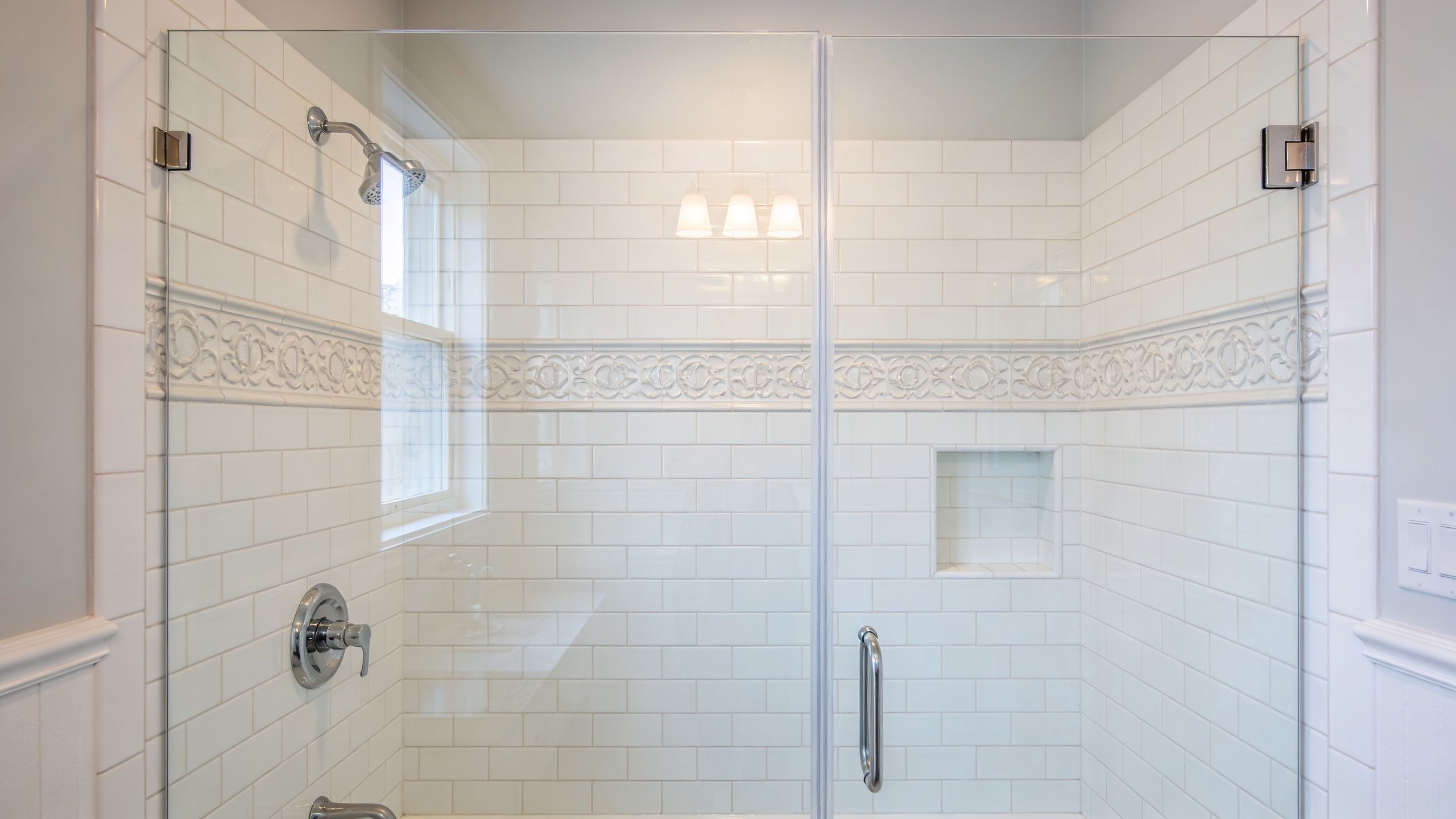 A clean, modern tiled shower stall featuring white subway tiles, a decorative accent band, and glass doors.