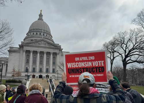 Speaker stands at a podium with crowd of supporters behind him