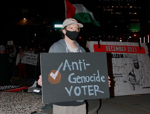 Speaker stands at a podium with crowd of supporters behind him
