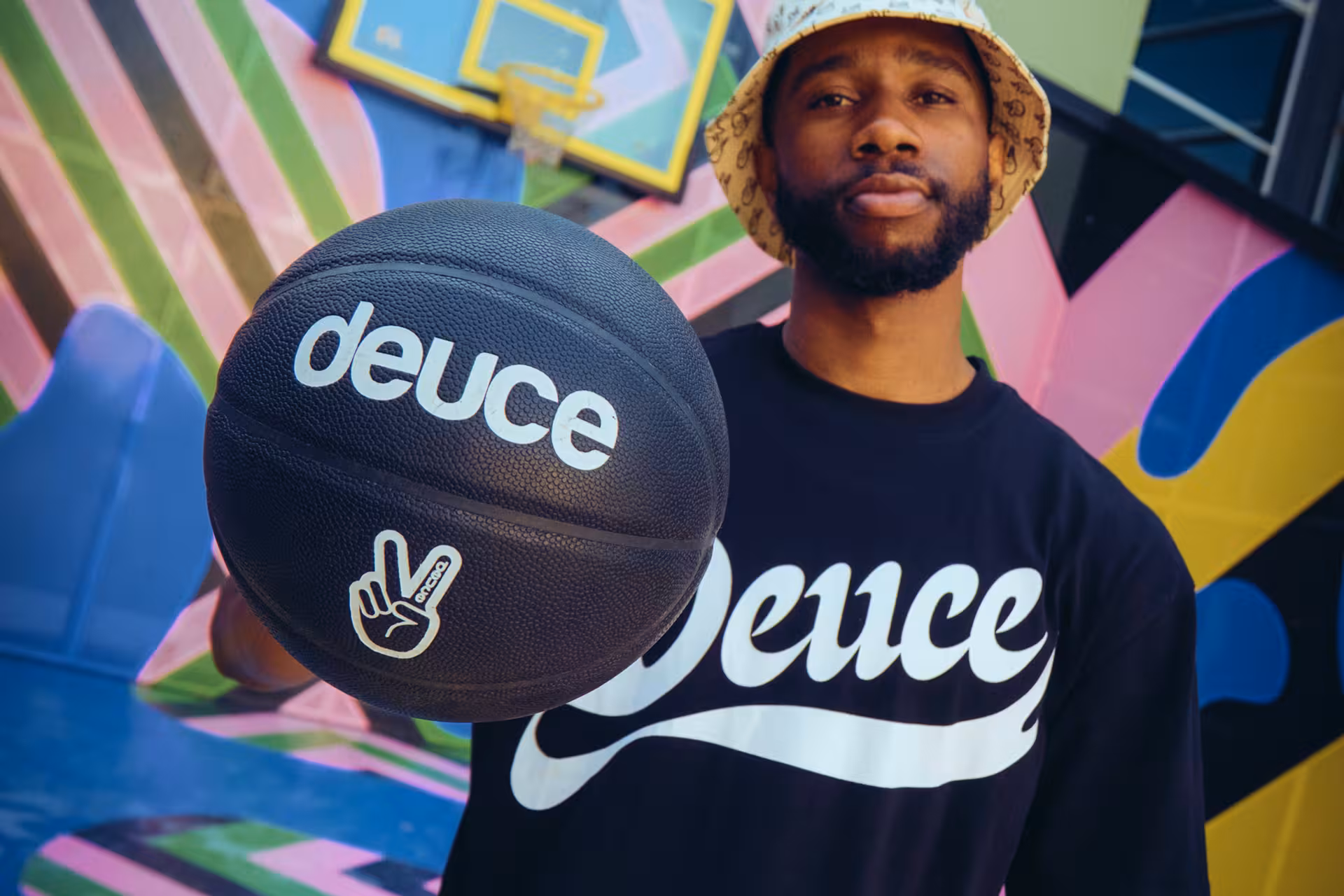 Man in Deuce branded clothing holds basketball against colorful geometric background