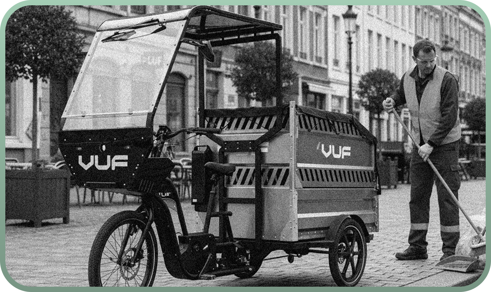 Man in a reflective vest sweeping a cobblestone street near a VUF electric cargo bike.