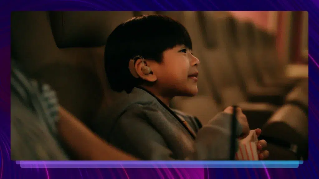 A young boy with a hearing aid enjoys a movie in a theater, enjoys a movie in a theater.