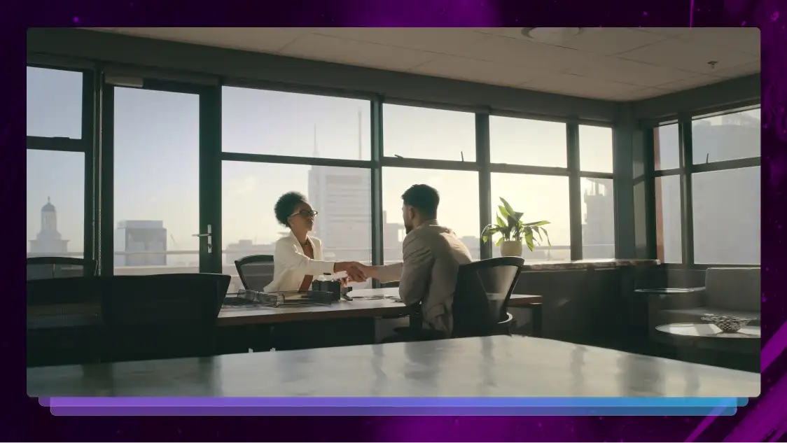 Two young lawyers shaking hands across a desk in a modern office with floor-to-ceiling windows overlooking a city skyline.