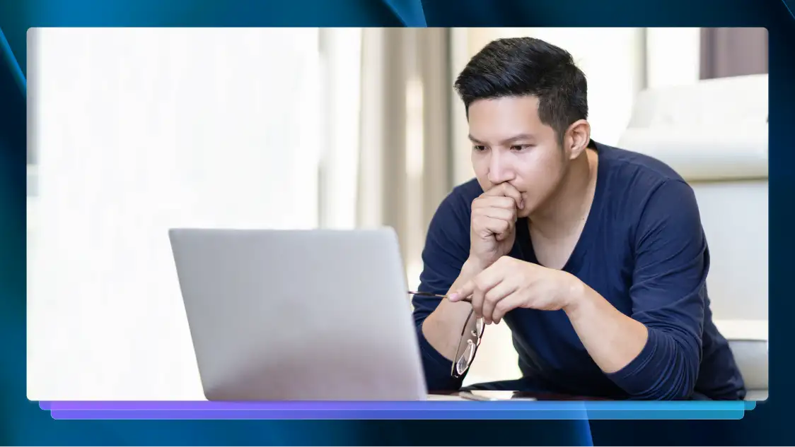 Man in navy shirt with glasses in hand, intently viewing a silver laptop.