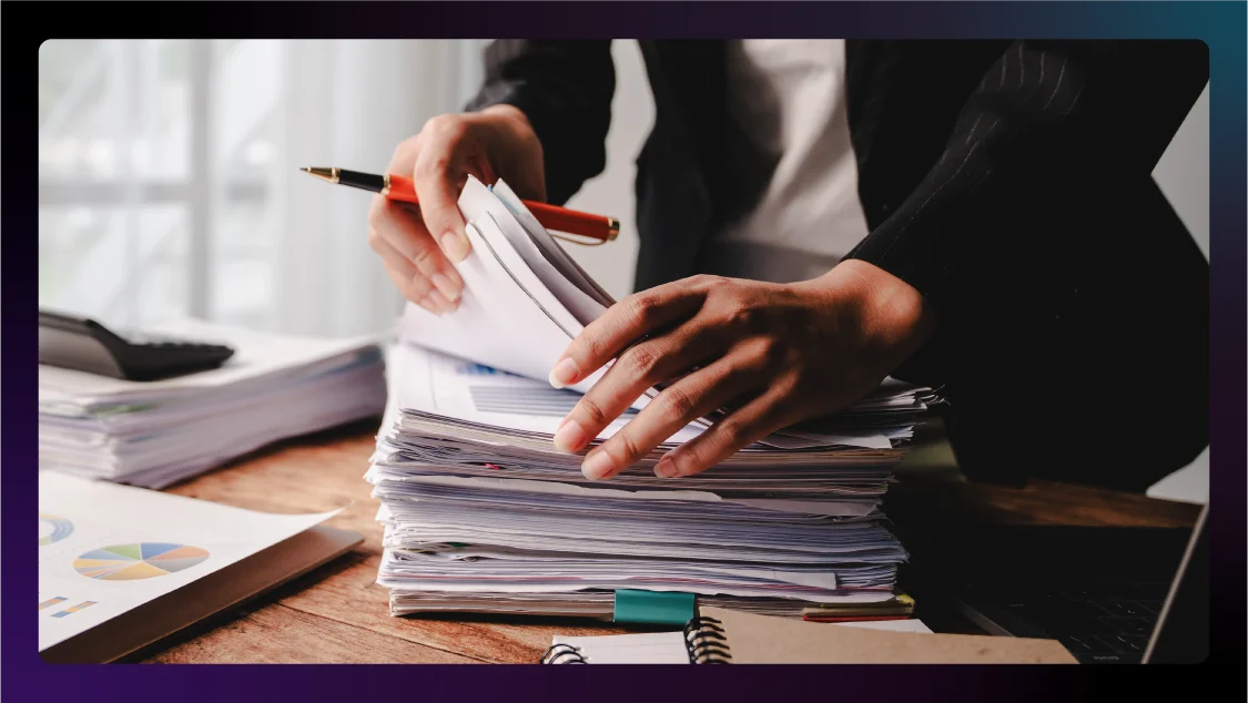 Close-up of a lawyer organizing a large stack of paperwork on a wooden desk.