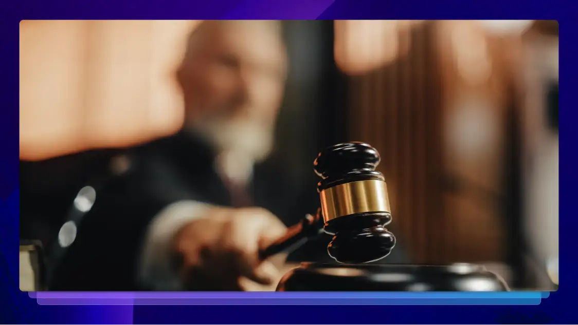 A judge is out of focus in the background. In focus is a gavel that the judge is holding in his hand.