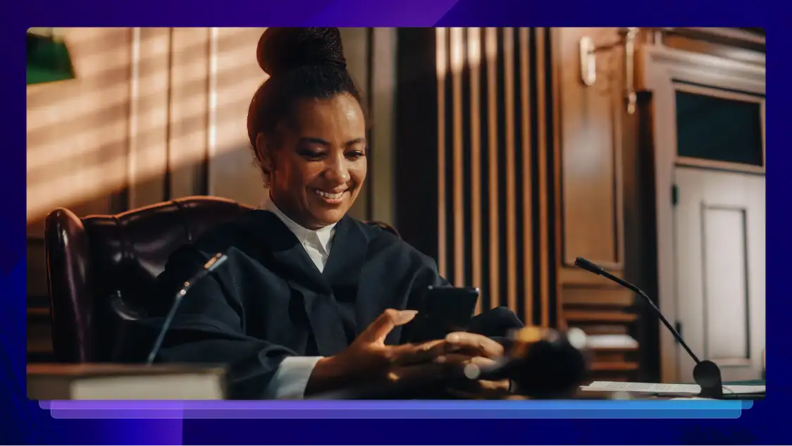 Judge looking at her phone and smiling in her seat at the head of a courtroom.