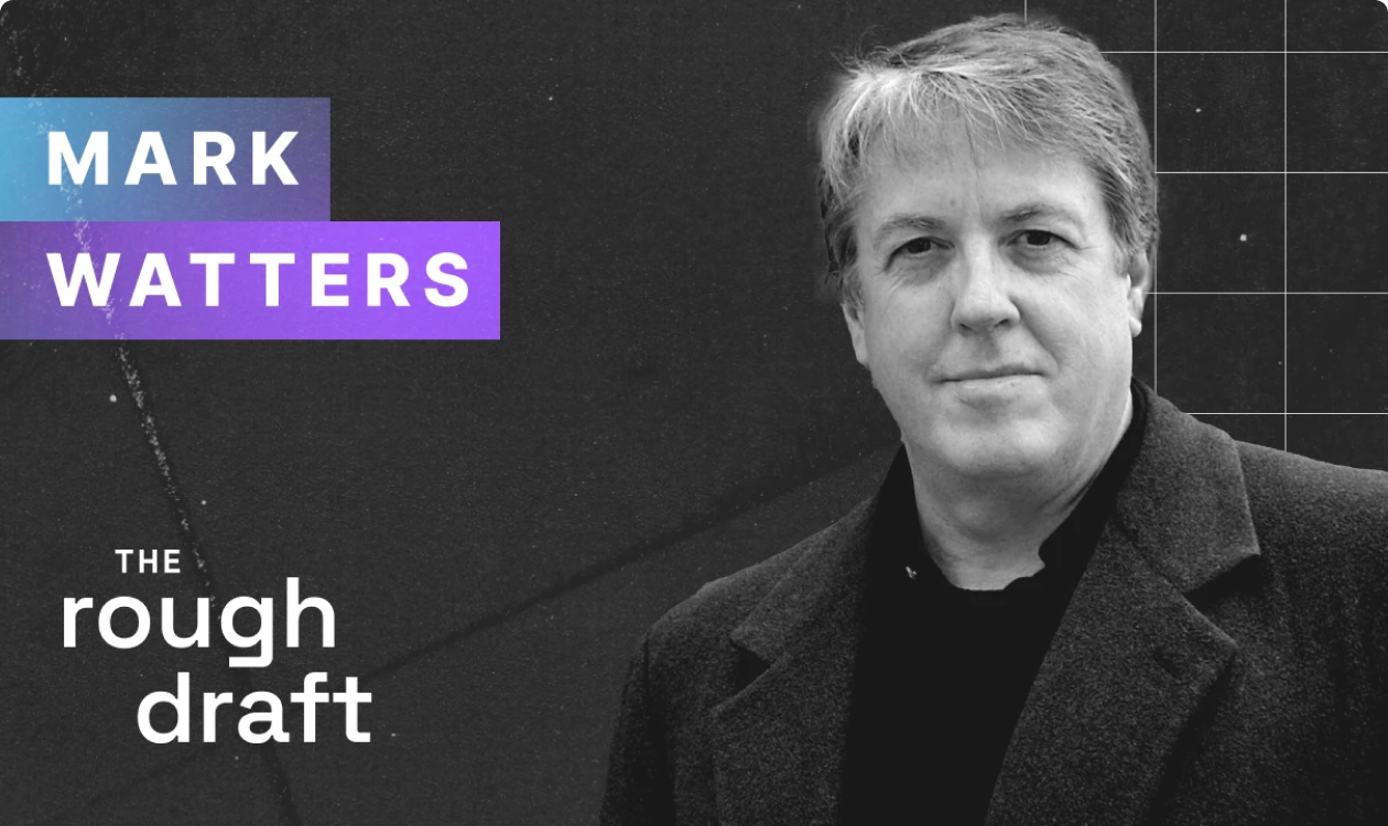 Headshot of professional smiling in suit jacket with neutral gray background, friendly portrait