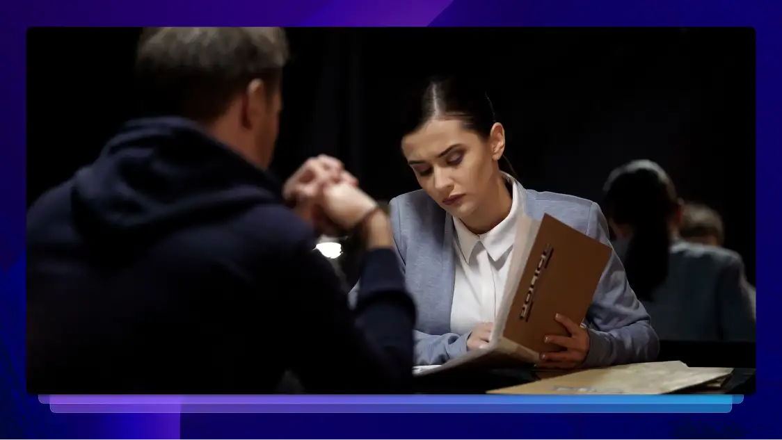 A lawyer sits across from a client in a dark room. She is looking at a folder of paperwork.