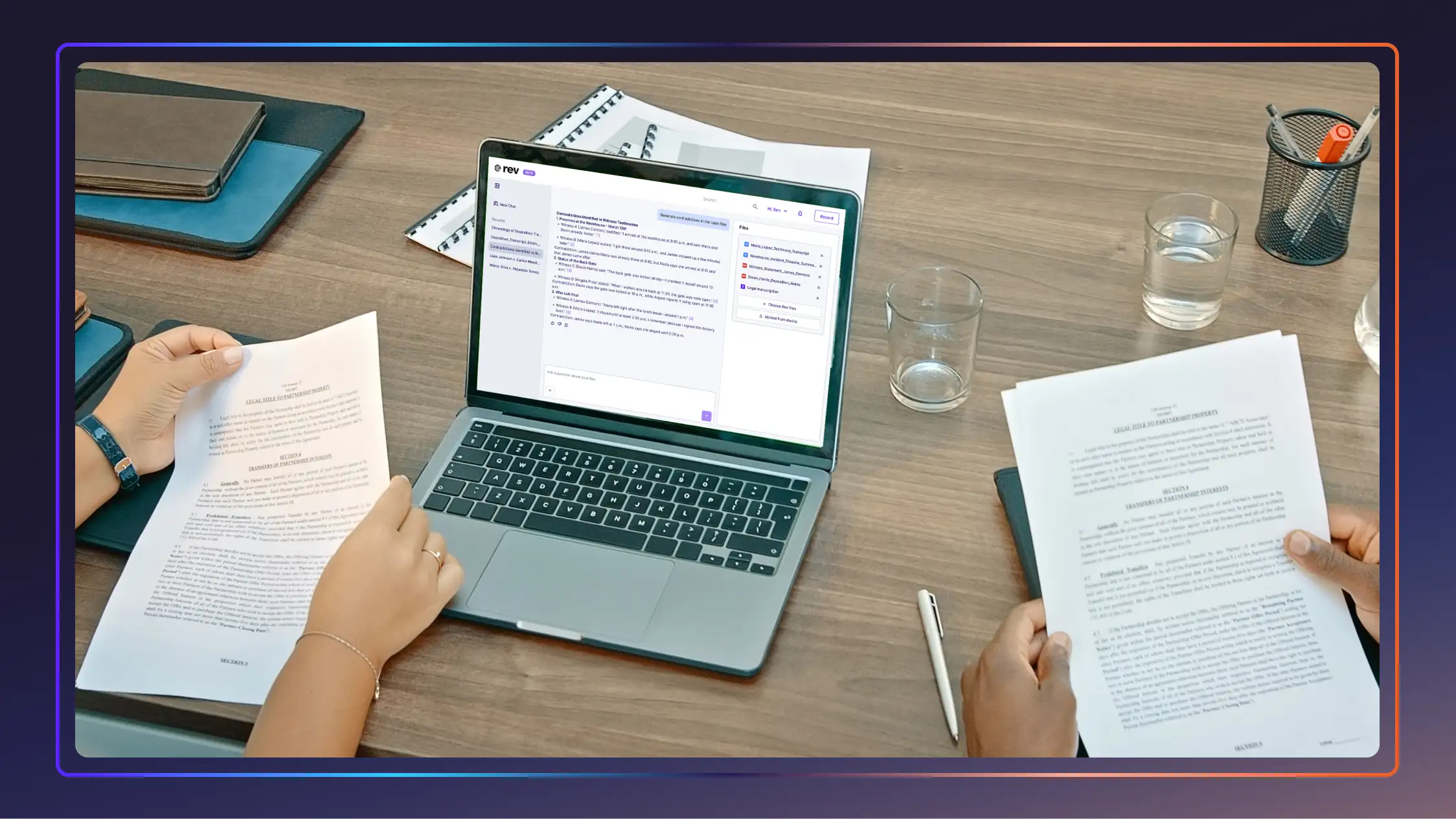 Two legal professionals working at a table with a laptop, legal documents, a pen, and two glasses of water.