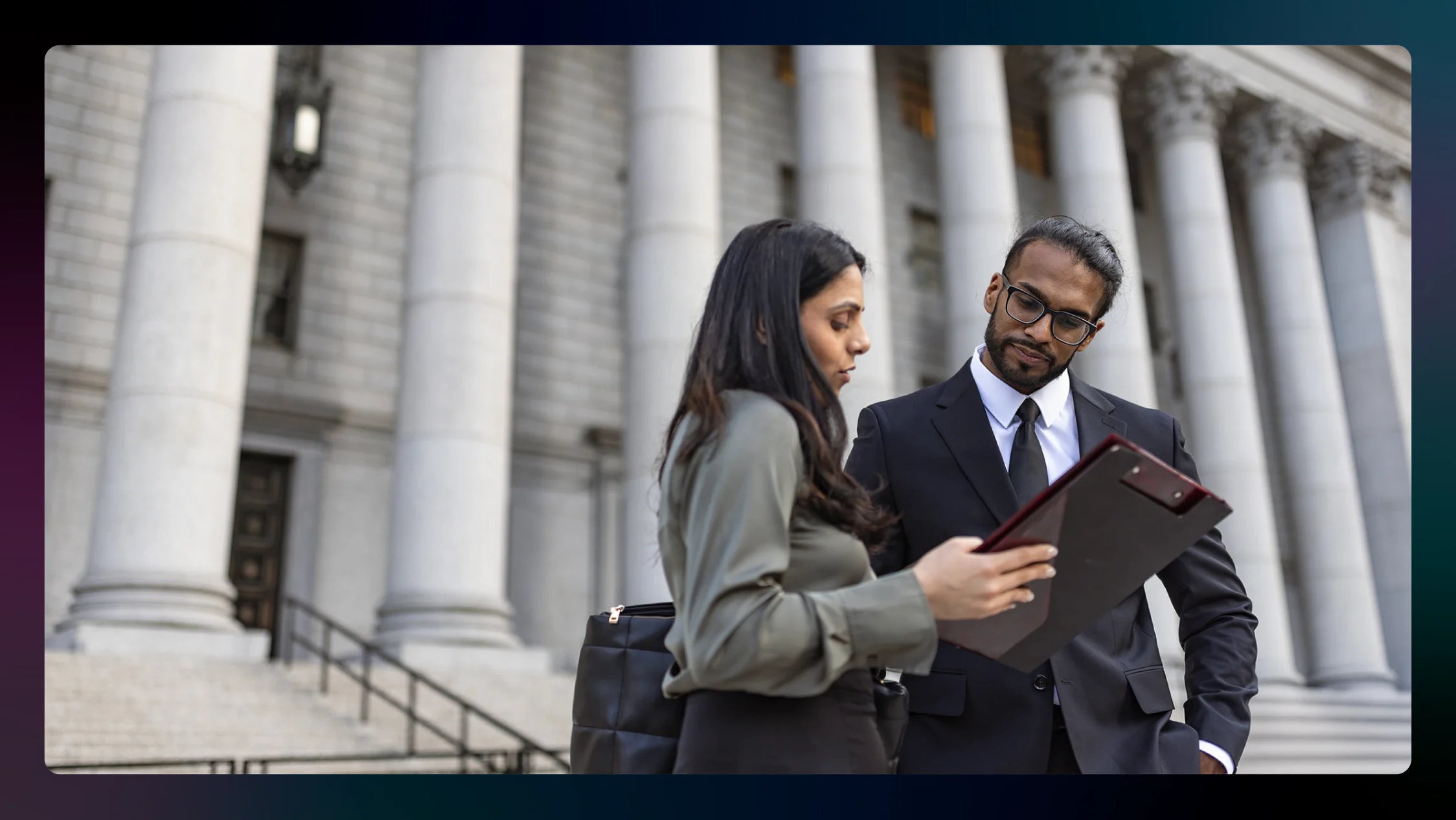 Two lawyers discuss a file while standing on courthouse steps.