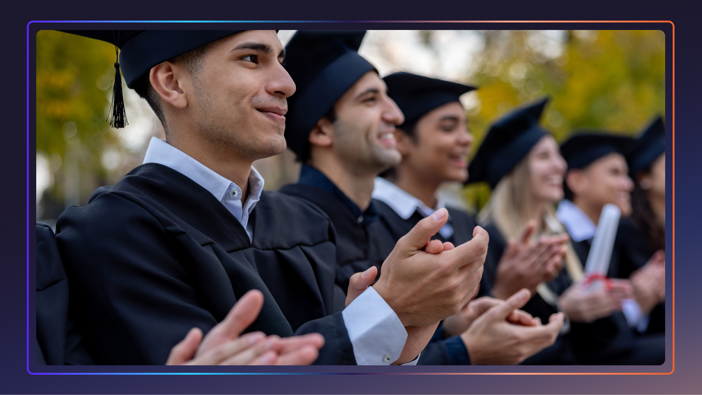 A group of students sits in a row in caps and gowns, clapping their hands during a commencement speech.