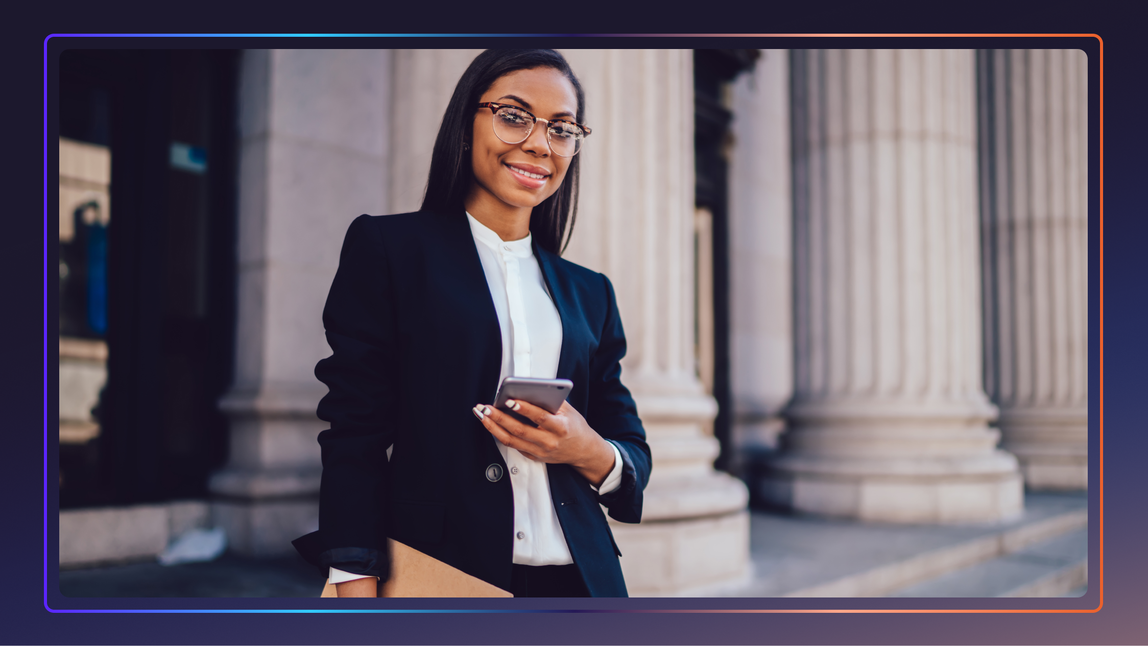 A young, African American female lawyer stands in front of a courthouse, smiling and holding a cell phone.