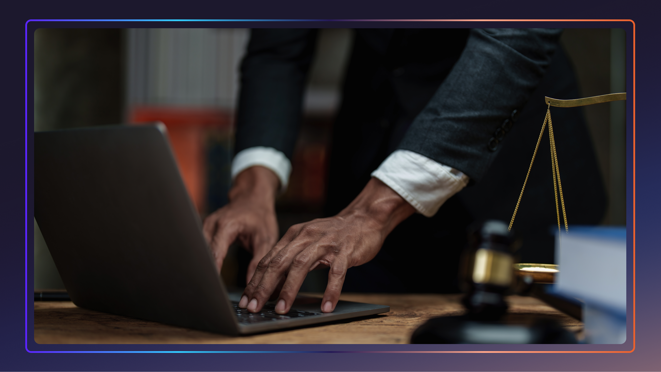 A man’s hands type on a laptop placed on a desk. He is wearing a suit.