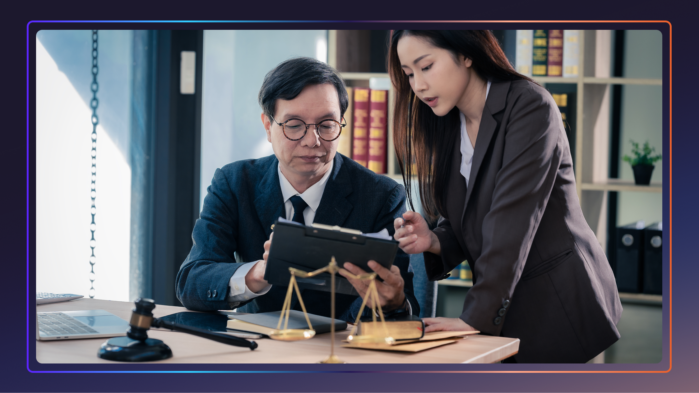 A man and a woman look and point at a clipboard. The man is sitting at a desk, and the woman is standing next to him.