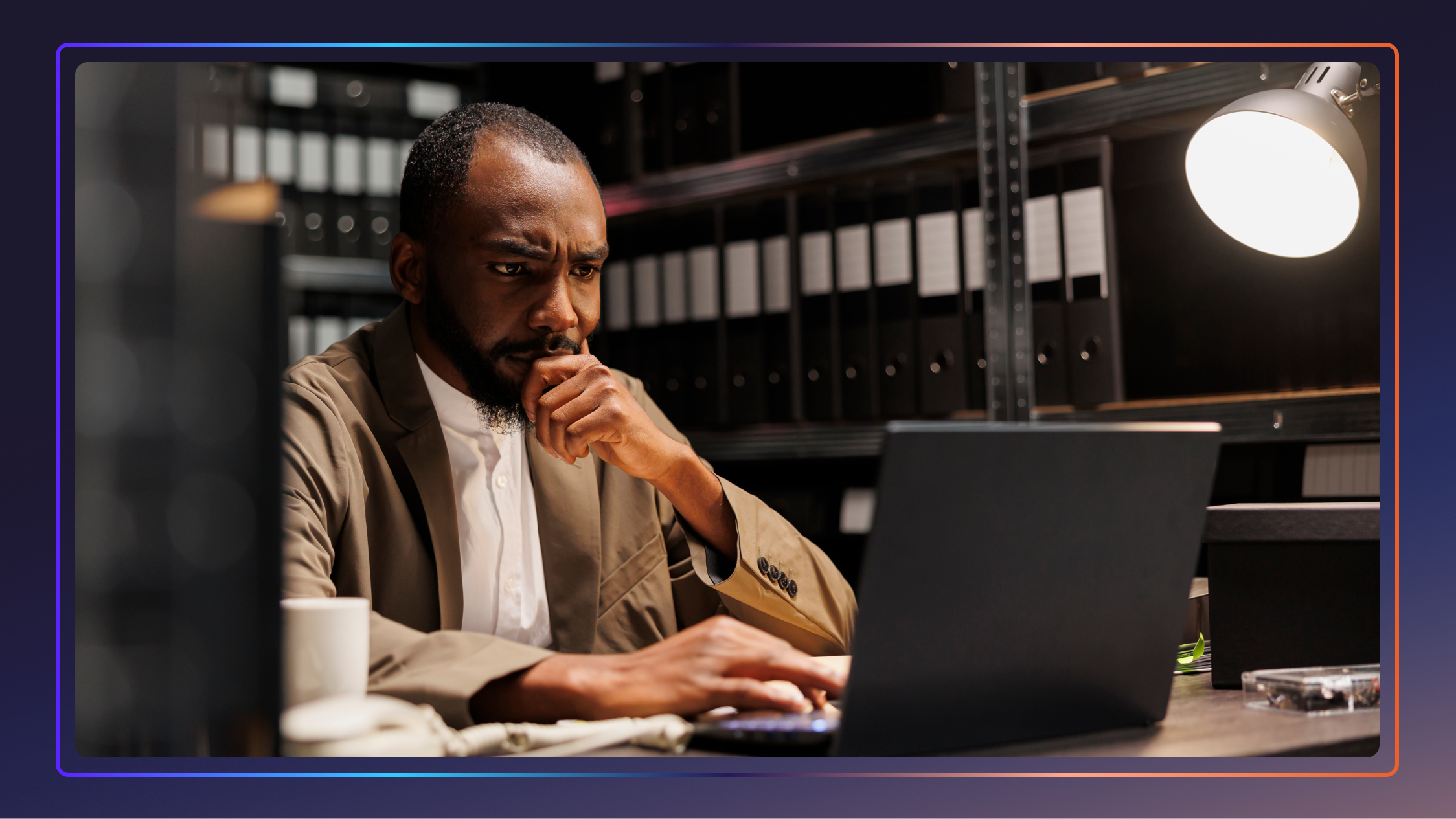 An investigator sits in a room and works on his laptop, he looks concerned.