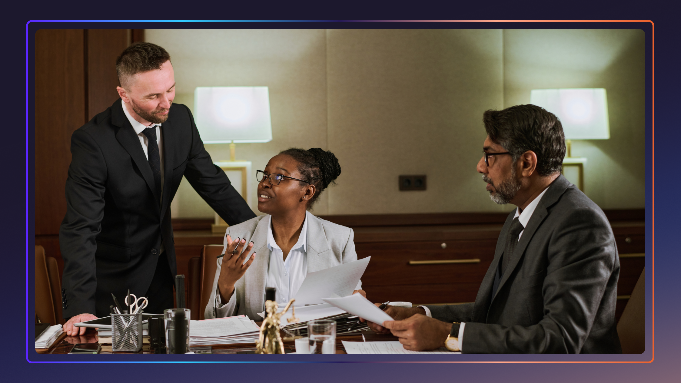 Two lawyers sit and talk to a third lawyer who is standing next to them.