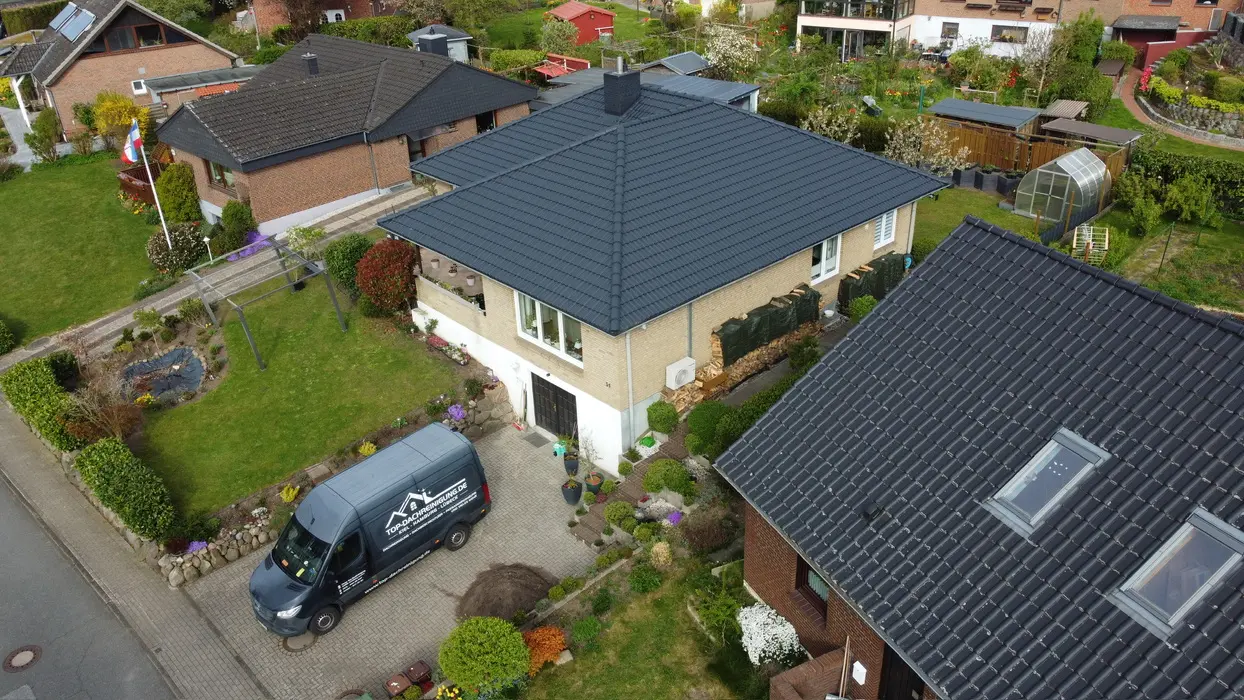 Luftaufnahme von Häusern mit frisch beschichtetem, sauberem Dach und geparktem Firmenfahrzeug.