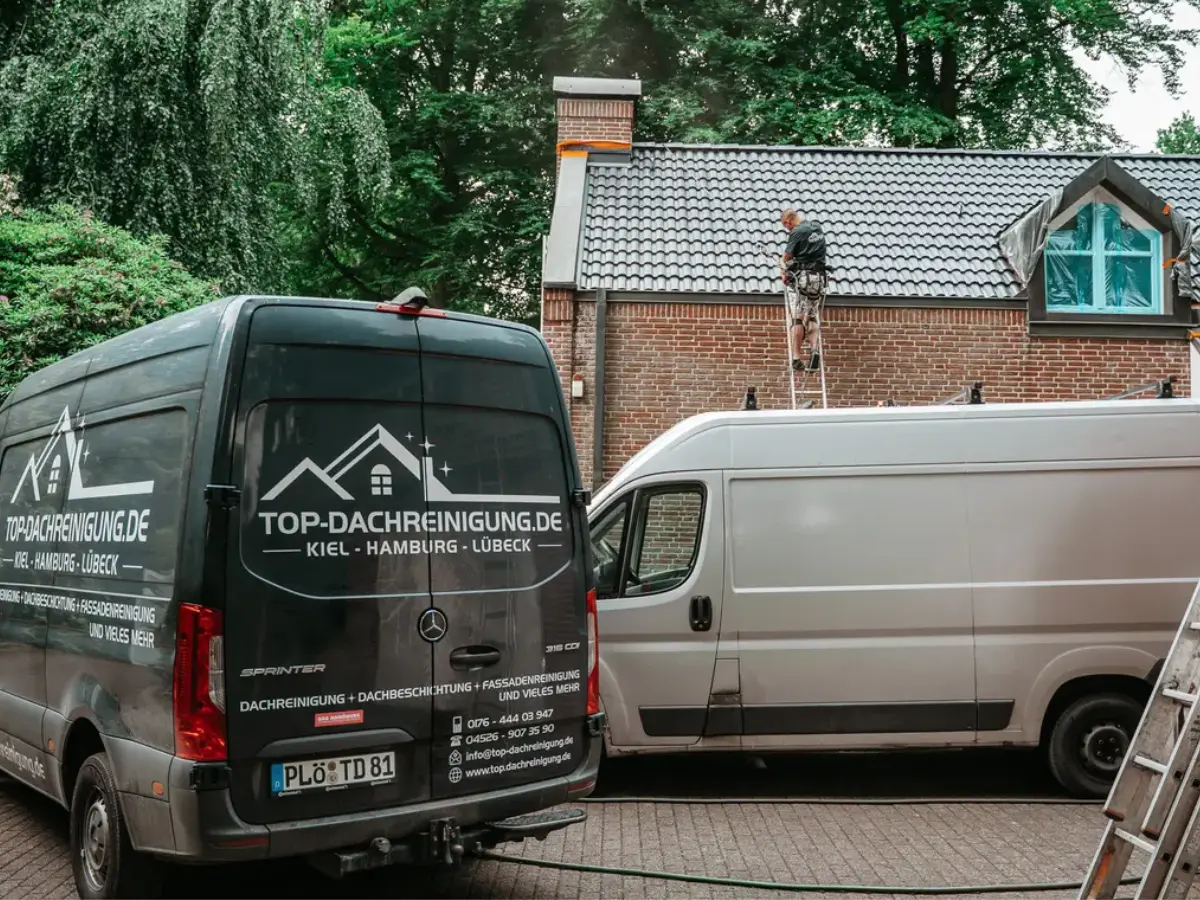Dachreinigung bei einem Wohnhaus mit Mitarbeiter und Servicefahrzeugen von Top-Dachreinigung vor Ort