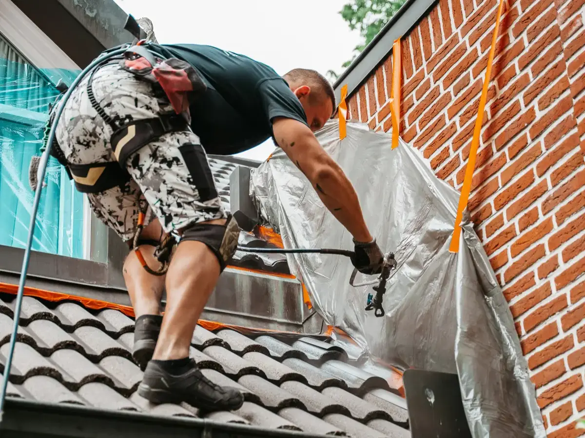 Mitarbeiter bei der Dachbeschichtung eines Wohnhauses mit professioneller Schutzbeschichtung der Dachziegel