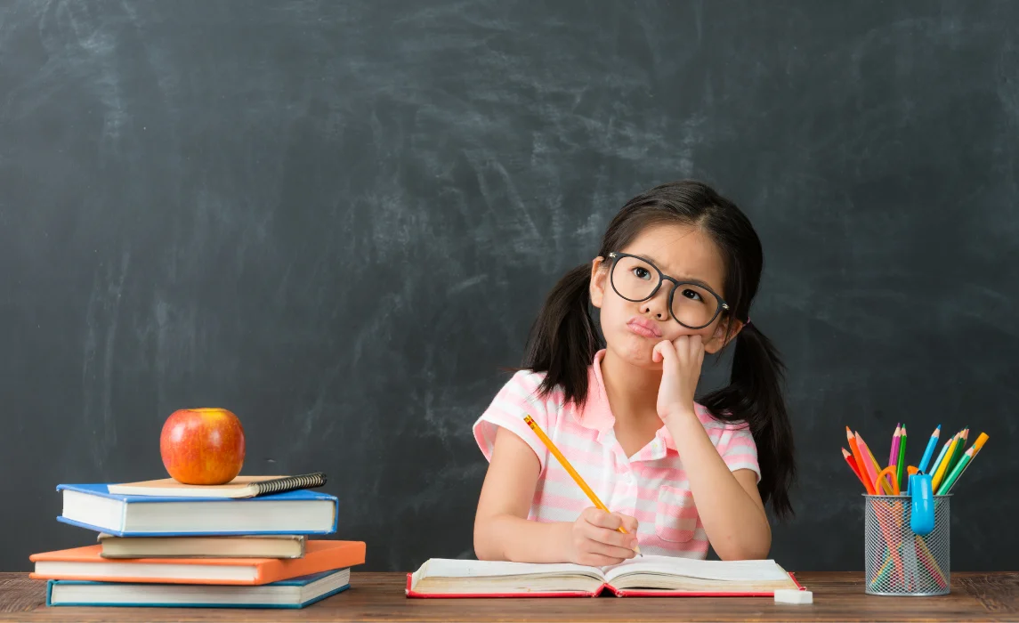 kid writing with her pencil with blackboard in the background