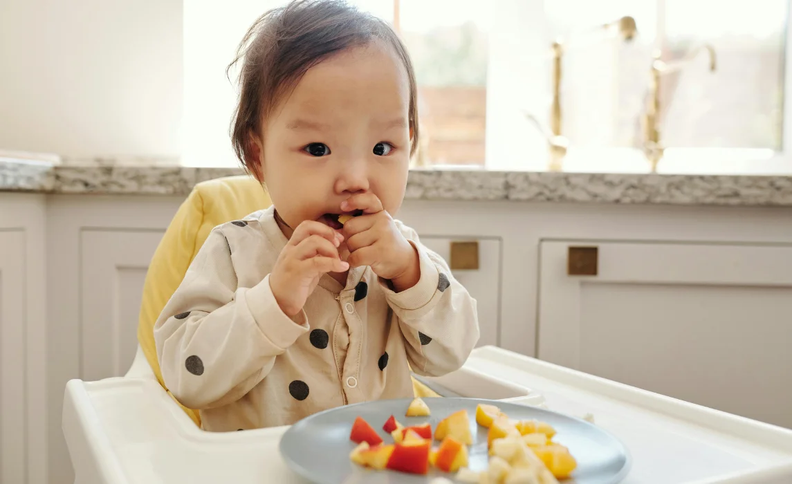 baby eating vegetable in its seat