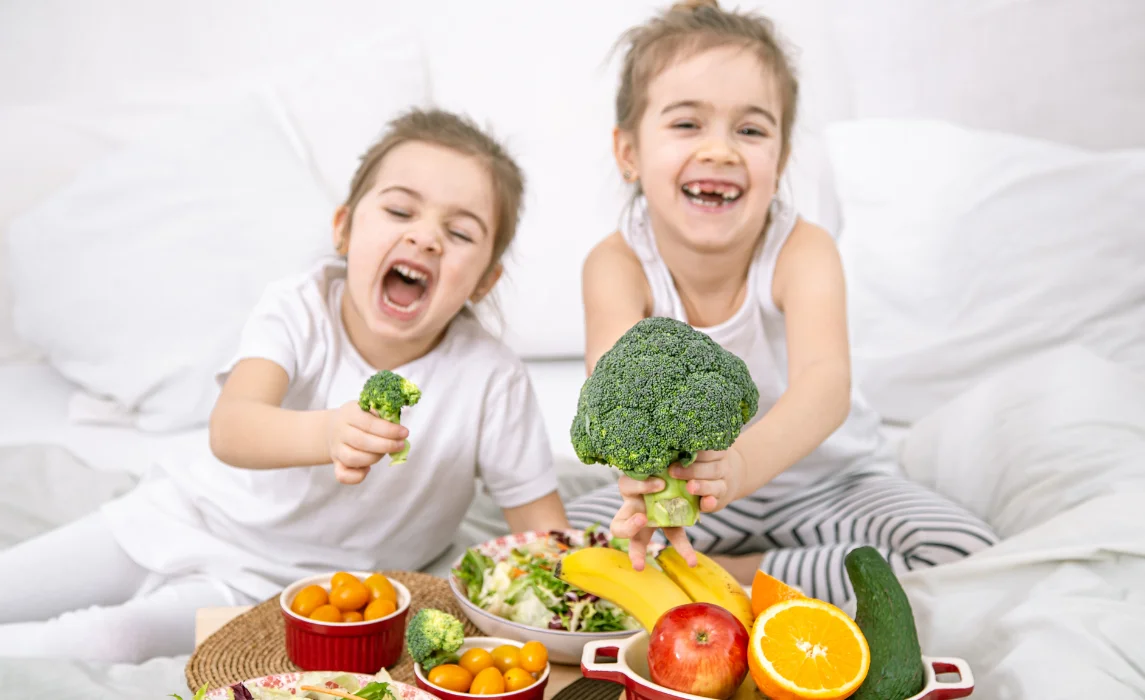 kids holding different sizes of broccoli in their bed
