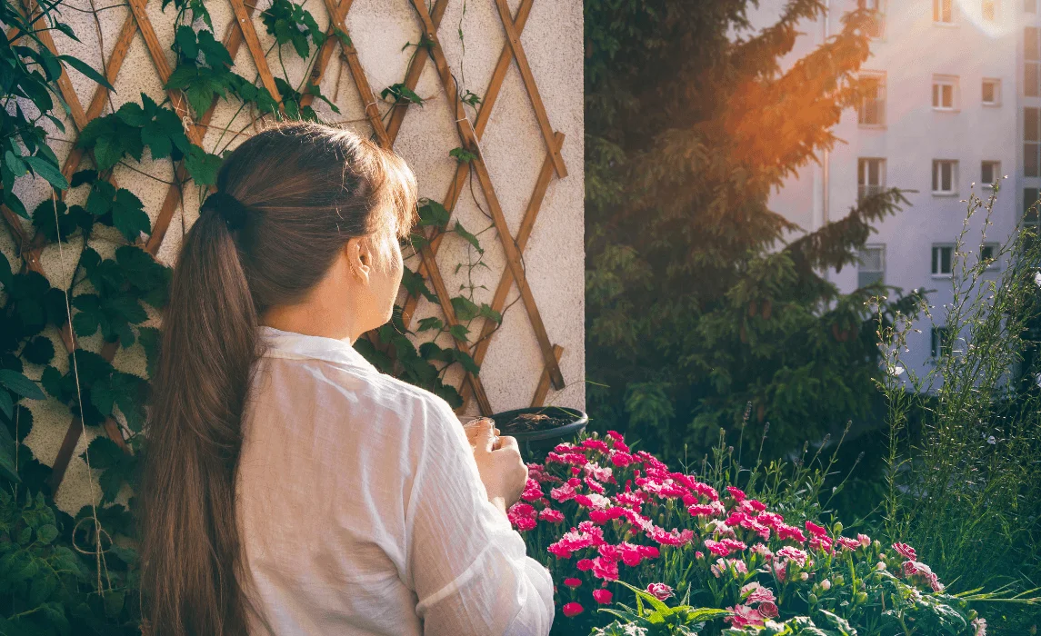 woman looking out balcony with plants and flowers under the sun