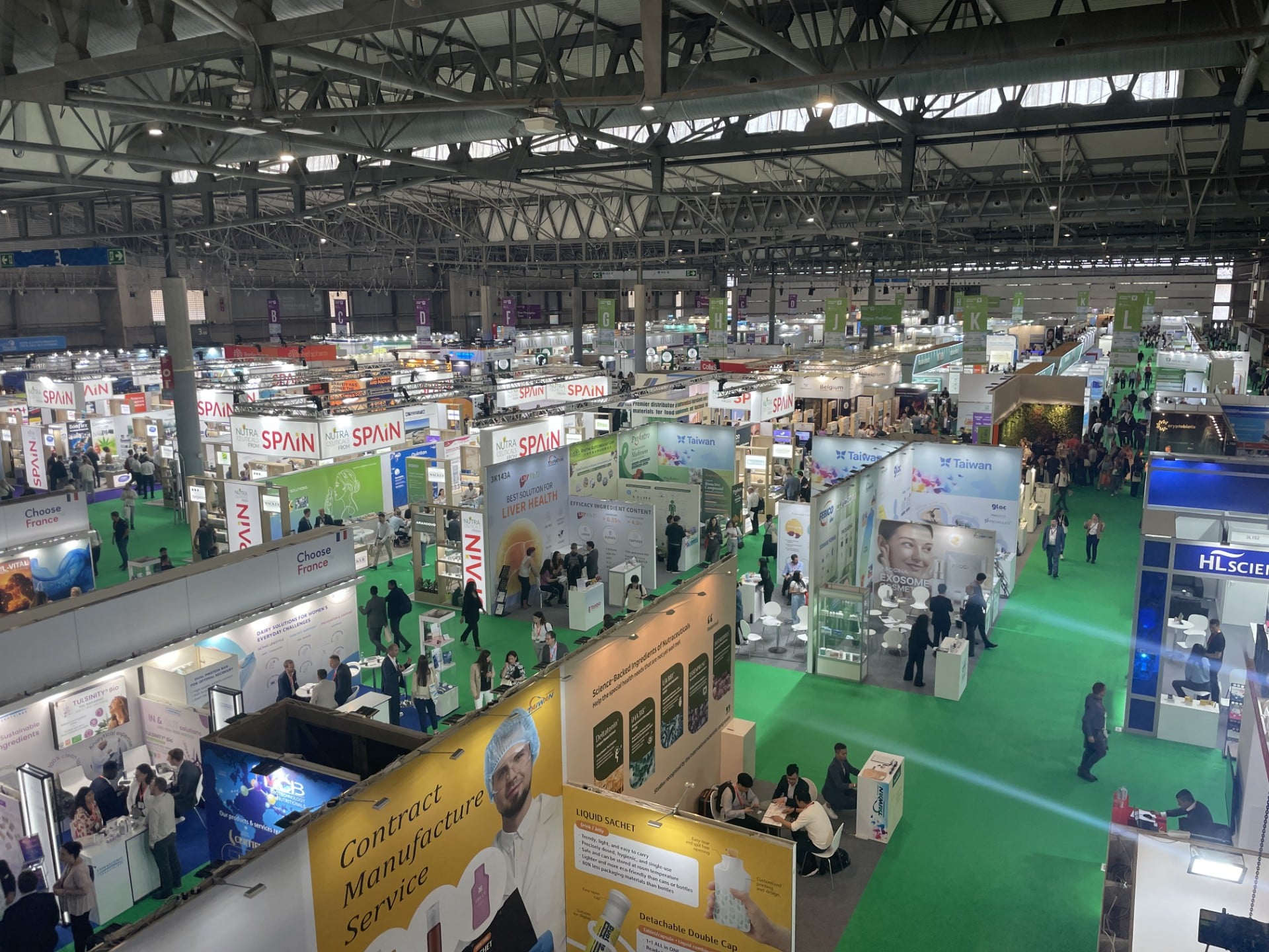 An image of the show floor at Vitafoods Europe 2025. Lots of brightly coloured and brightly lit stands sit on a green carpet in an exhibition hall 
