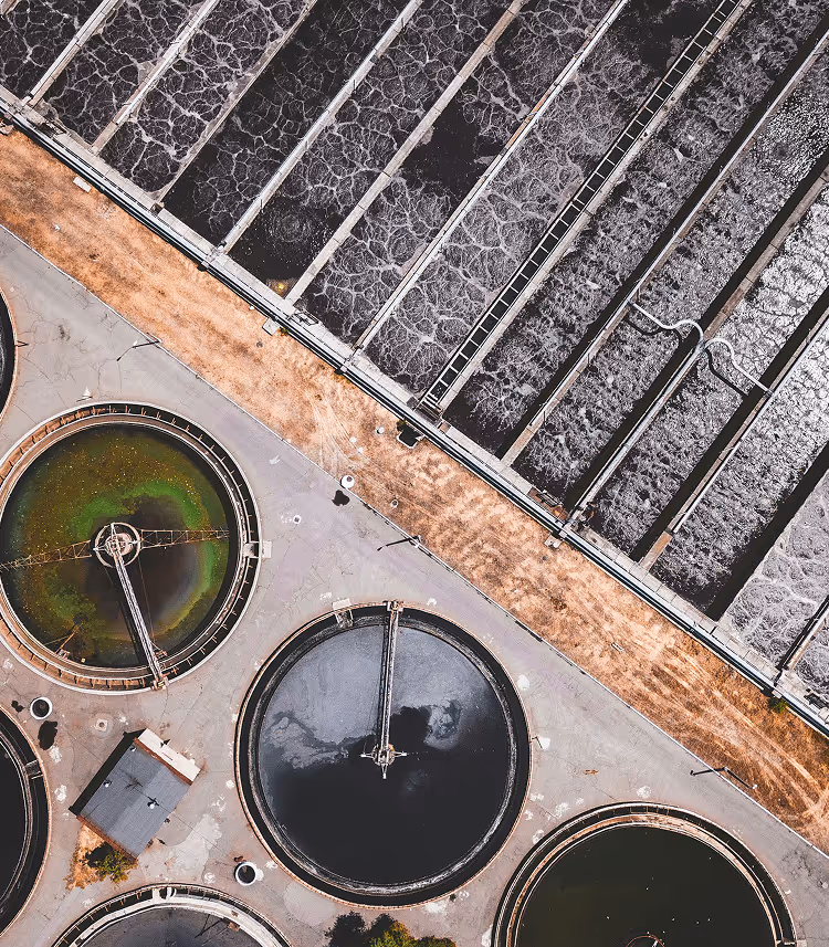 Luchtfoto van grote ronde en rechte watertanks bij een waterzuiveringsinstallatie.
