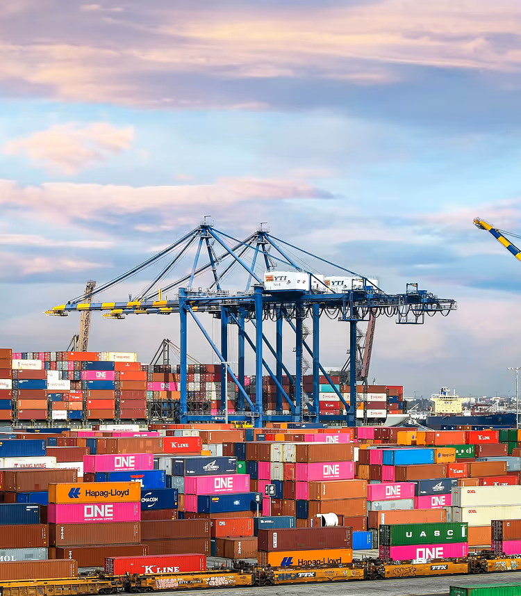 Containerterminal met gestapelde kleurrijke containers en grote zeehavenkranen onder een bewolkte hemel.