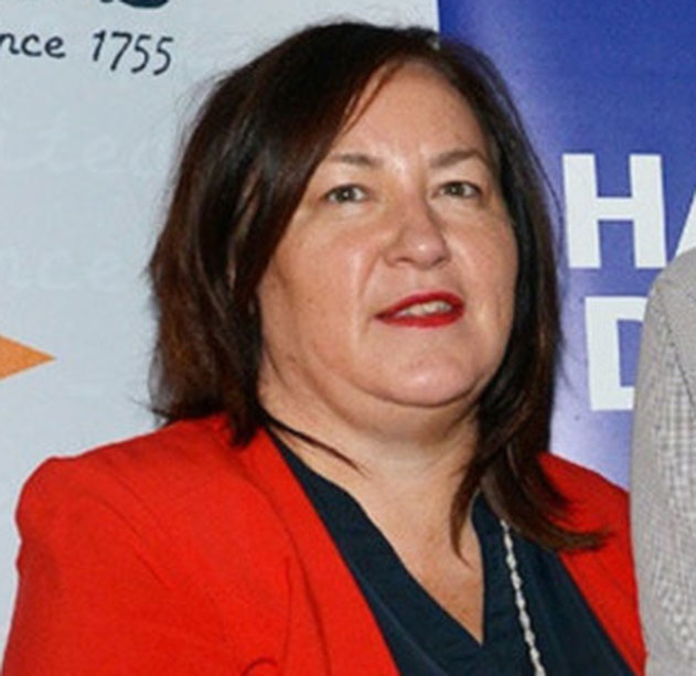 Woman with short dark hair and bangs holding a small vintage camera up to one eye, wearing a blue shirt with a bird pattern, neutral background.