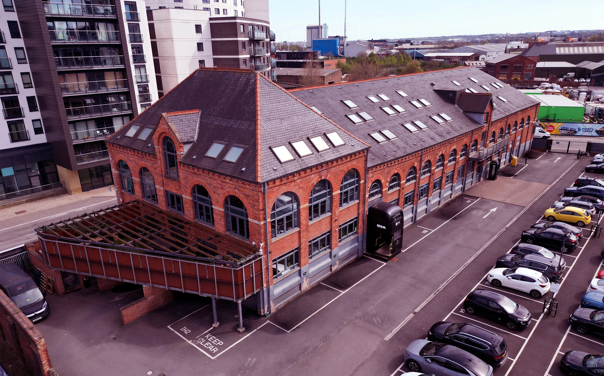The Malthouse in Leeds with arched windows and many skylights, next to a parking lot with multiple cars.