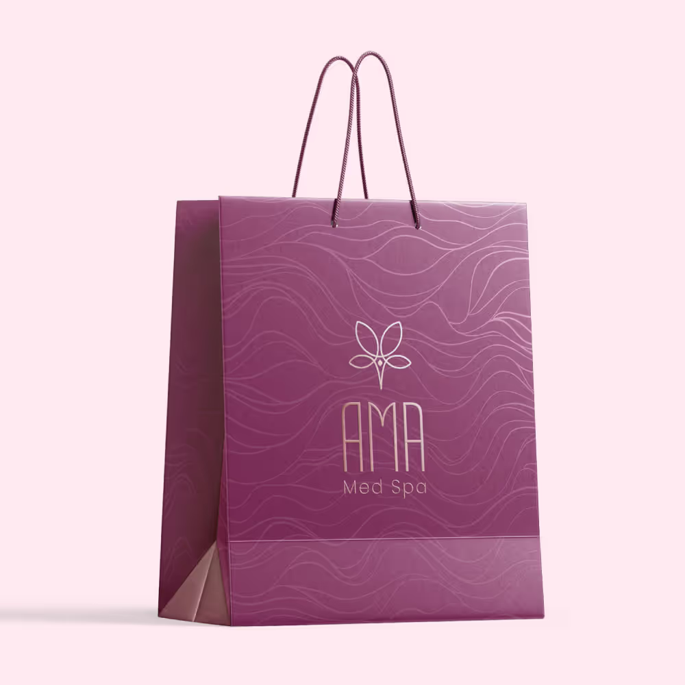Branded shopping bag design for AMA Med Spa featuring a deep mauve color and a subtle wavy line pattern in the background, symbolizing elegance and flow. The AMA logo, with its butterfly motif and modern typography, is prominently displayed in a soft metallic finish, paired with the text 'Med Spa' underneath. The bag's handles are crafted in a matching mauve tone, reinforcing the cohesive and luxurious branding.